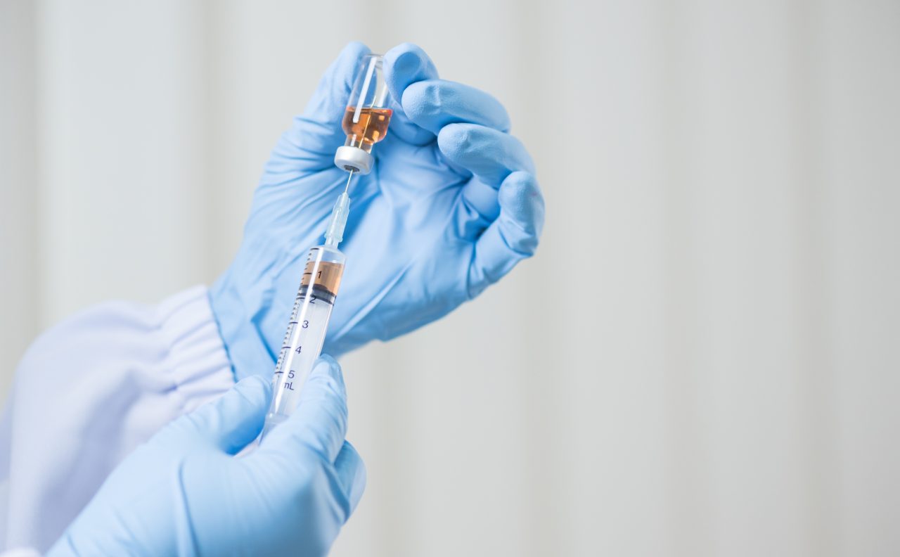 Close up doctor's hand holding medicine bottle and syringe for vaccine to patient on blue tone